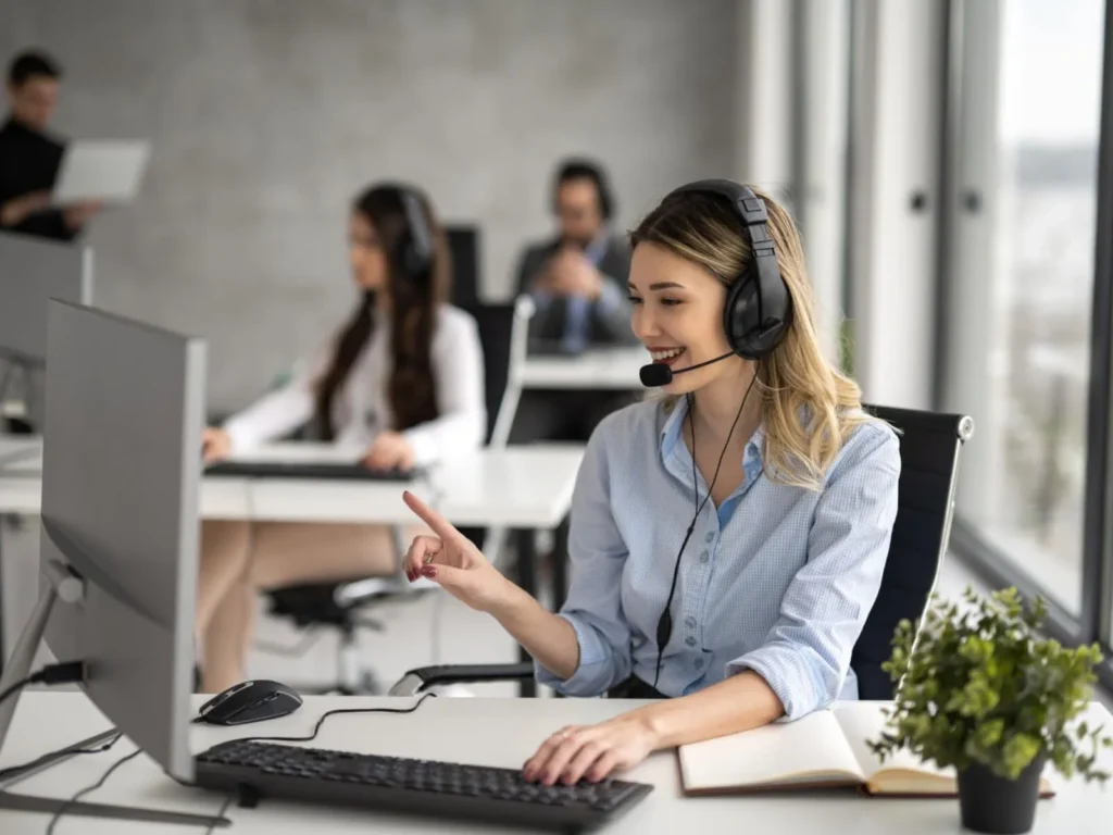 A woman with a headset looking at a computer whilst answering the phone